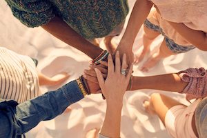 Group of young men and women showing unity. Group of young friends putting their hands together at the beach.