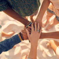Group of young men and women showing unity. Group of young friends putting their hands together at the beach.